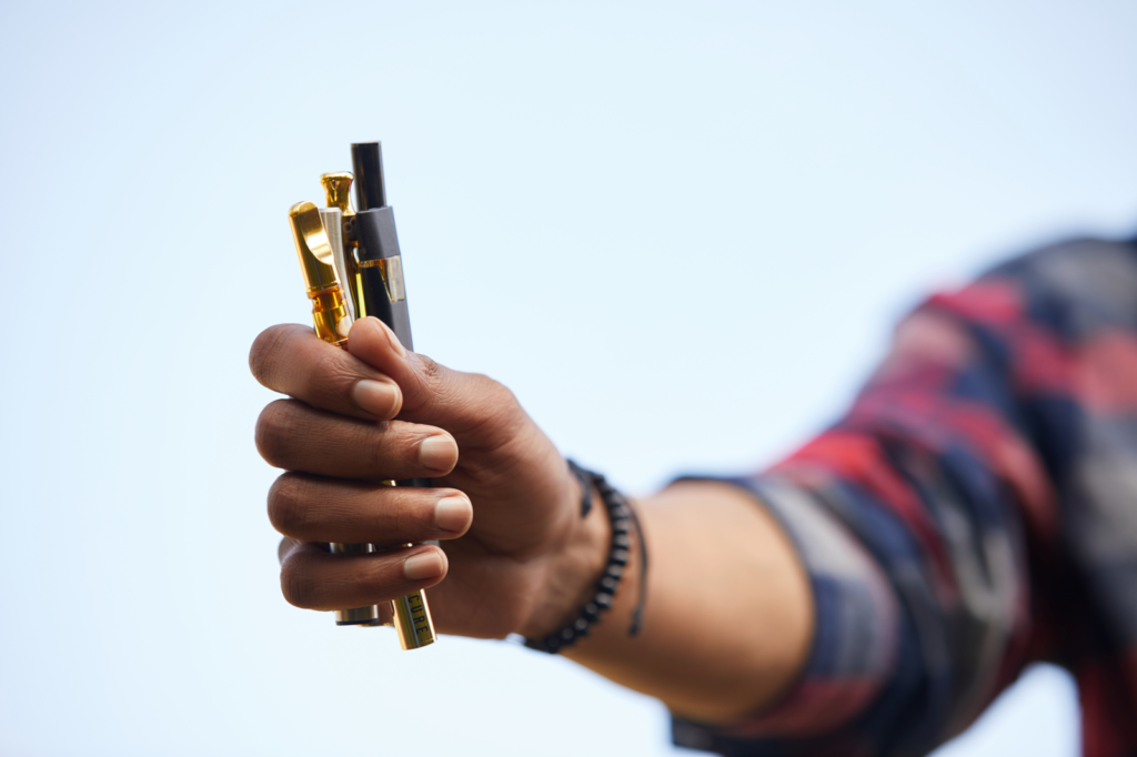 Hand holding multiple THC cartridges outdoors against a clear sky, showing a variety of product options
