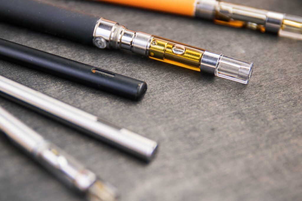 Close-up detail of a 510-thread THC cartridge showing the heating element and concentrated cannabis extract inside, with battery hardware in the background.