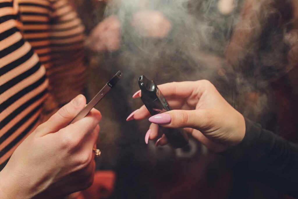 Two hands exchanging and comparing different THC vape devices, showing lifestyle use and product comparison